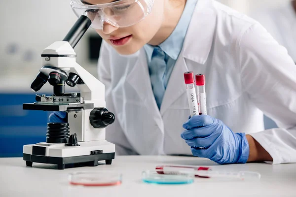 Vista recortada del consultor genético utilizando microscopio y tubos de ensayo de retención — Stock Photo