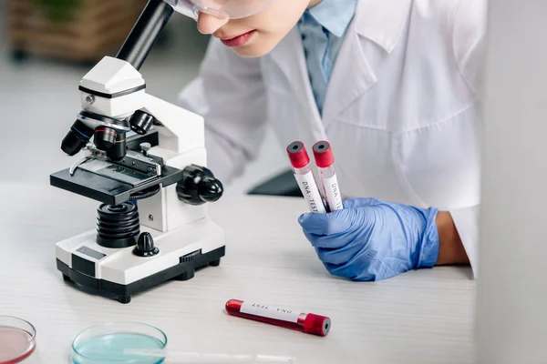 Vista recortada del consultor genético utilizando microscopio y tubos de ensayo de retención - foto de stock