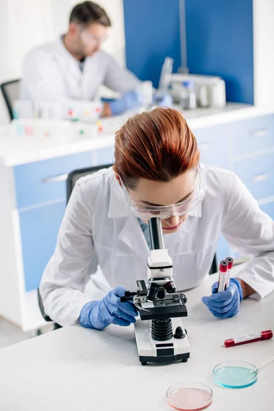 Selective focus of genetic consultant holding test tubes and using microscope in lab — Stock Photo