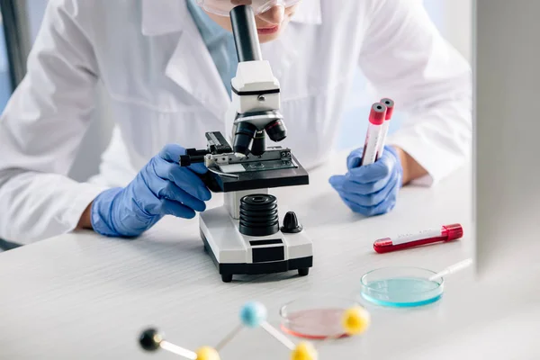 Vista recortada del consultor genético utilizando microscopio y tubos de ensayo de retención - foto de stock