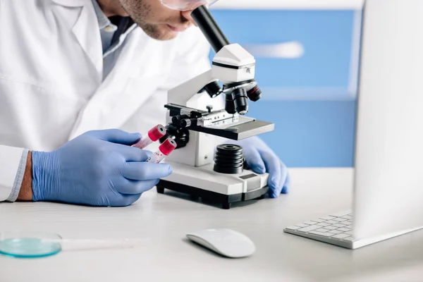 Vista recortada del consultor genético que sostiene tubos de ensayo y utiliza microscopio - foto de stock