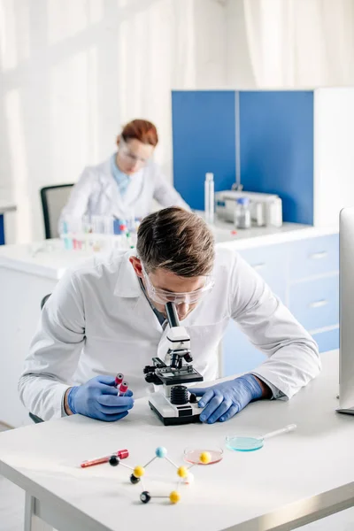 Foco seletivo de consultores genéticos segurando tubos de ensaio e usando microscópio em laboratório — Fotografia de Stock