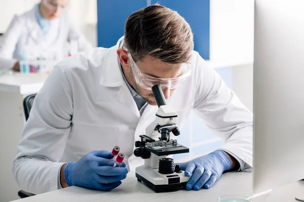 Genetic consultant holding test tubes and using microscope in lab — Stock Photo