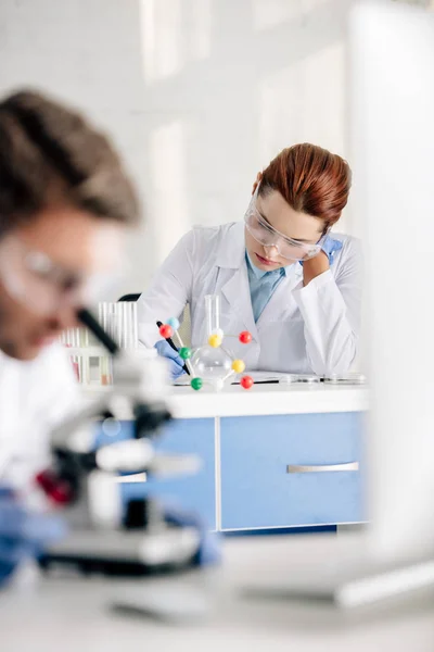 Selective focus of genetic consultant writing and colleague using microscope in lab — Stock Photo