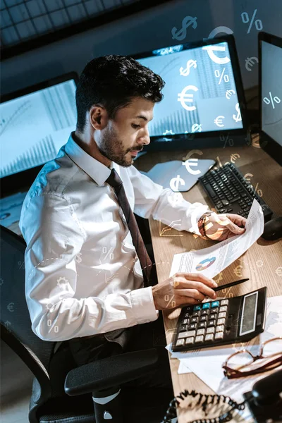 Bi-racial trader using calculator and holding charts and graphs near money signs — Stock Photo