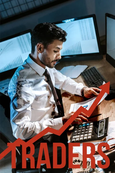 Bi-racial man using calculator and holding charts and graphs near traders letters — Stock Photo