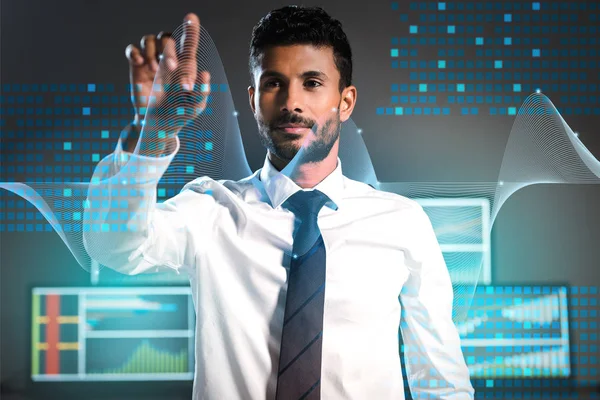 Enfoque selectivo del comerciante bi-racial señalando con el dedo cerca de las computadoras en el fondo - foto de stock