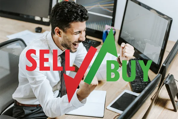 Happy bi-racial trader showing yes gesture near computers, sell and buy letters — Stock Photo