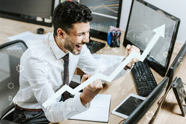 Glücklicher bi-rassischer Händler, der Ja-Geste in der Nähe von Computern zeigt und Grafiken erhebt — Stockfoto