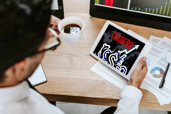 Selective focus of man holding cup and digital tablet with traders letters — Stock Photo