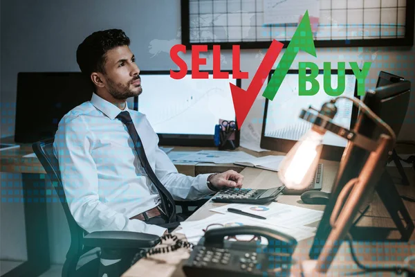 Pensive bi-racial trader sitting near computers, sell and buy letters — Stock Photo