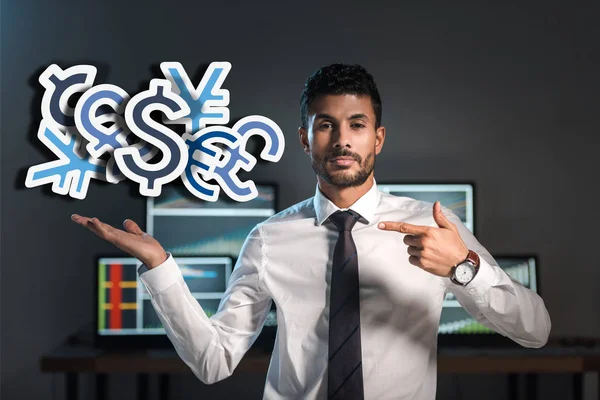 Bi-racial trader pointing with finger at money signs near computes — Stock Photo