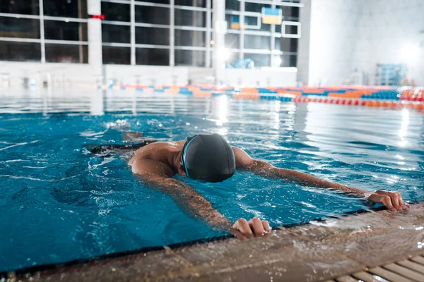 Hombre en gorra de natación estiramiento en agua - foto de stock
