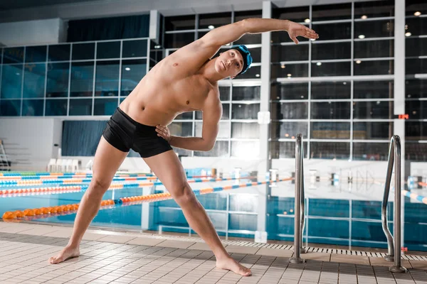 Hombre guapo en la gorra de natación calentamiento cerca de la piscina - foto de stock