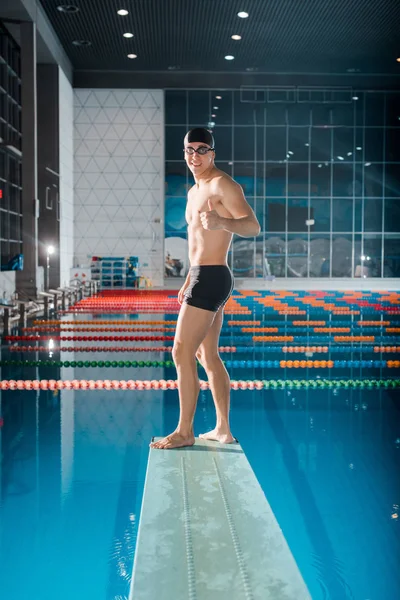 Nadador feliz mostrando el pulgar hacia arriba mientras está de pie en el trampolín - foto de stock