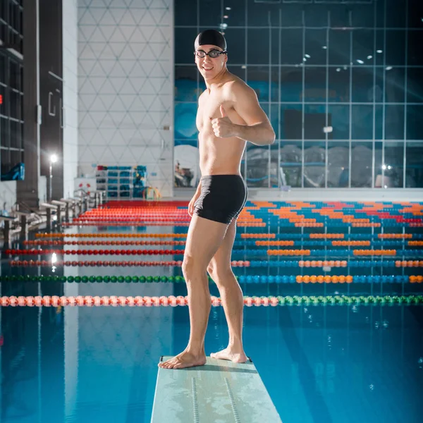 Smiling swimmer showing thumb up while standing on diving board — Stock Photo