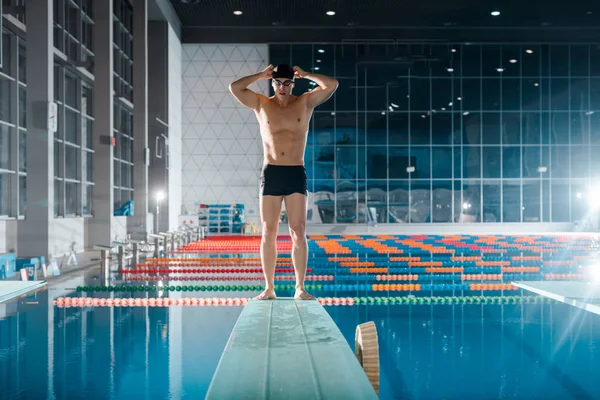 Guapo y musculoso nadador tocando gorra de natación cerca de la piscina - foto de stock