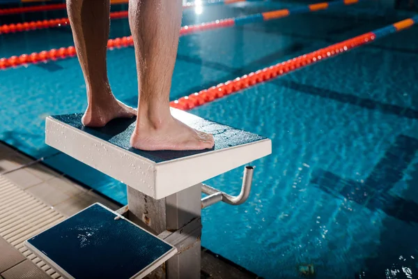 Vista recortada del deportista de pie en el bloque de buceo cerca de la piscina - foto de stock