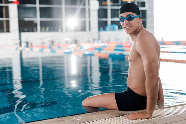 Nadador sonriente con gafas sentado cerca de la piscina - foto de stock