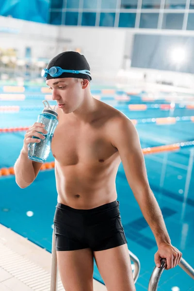 Guapo nadador sosteniendo botella deportiva cerca de la piscina - foto de stock