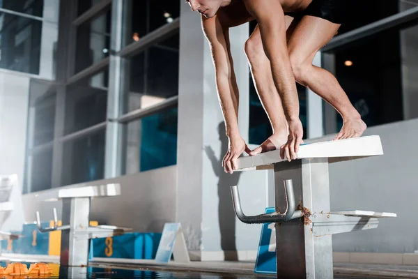 Cropped view of sportsman standing in starting pose on diving block — Stock Photo