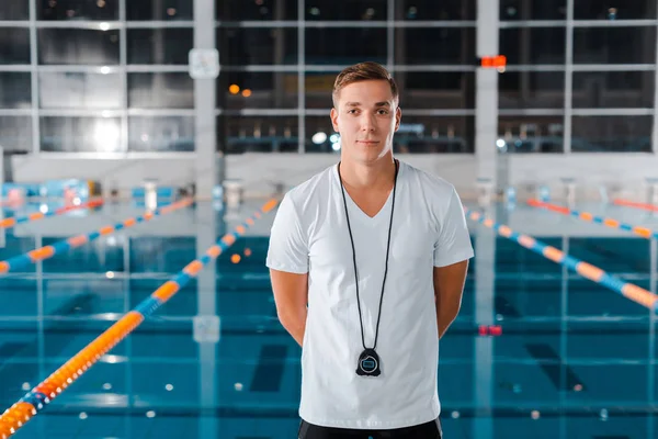 Entrenador alegre mirando a la cámara mientras está de pie cerca de la piscina — Stock Photo