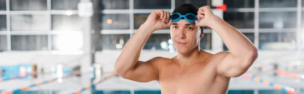 Tiro panorámico de nadador atlético feliz tocando gafas - foto de stock