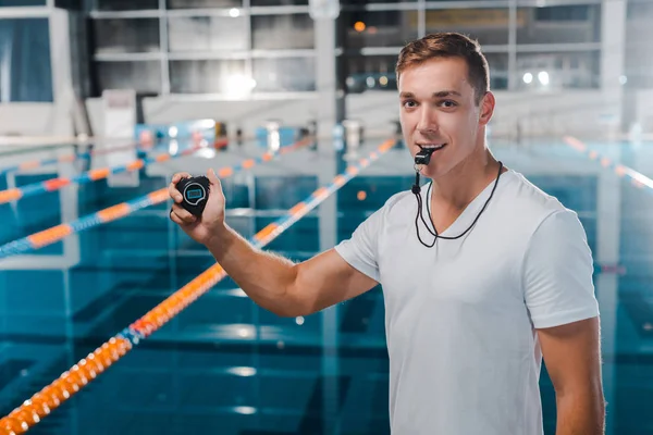 Smiling trainer with timer in hand holding whistle in mouth — Stock Photo