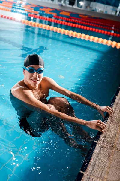 Happy swimmer in goggles smiling while looking at camera in swimming pool — Stock Photo