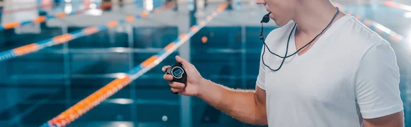 Panoramaaufnahme eines Trainers im weißen T-Shirt, der auf die Uhr schaut, während er die Trillerpfeife im Mund hält — Stockfoto