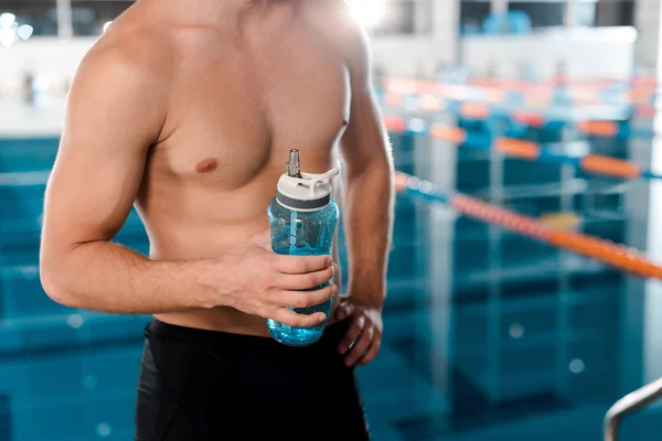 Vista cortada de desportista muscular segurando garrafa de esportes perto da piscina — Fotografia de Stock