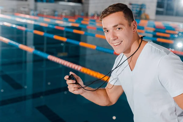 Fröhlicher Trainer hält Zeitschaltuhr in der Hand und blickt in die Kamera am Schwimmbad — Stockfoto