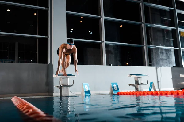 Schöner und hemdsloser Schwimmer, der in Startpose auf dem Sprungblock steht — Stockfoto
