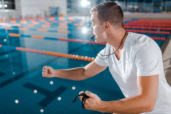 Entraîneur émotionnel avec sifflet dans la bouche gestuelle tout en regardant la piscine — Photo de stock