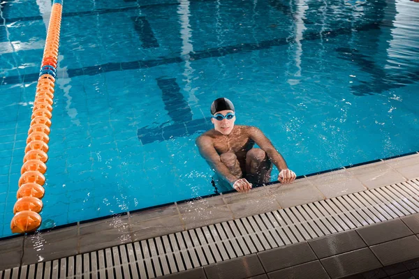 Belo nadador em touca de natação olhando para câmera na piscina — Fotografia de Stock
