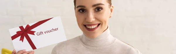 Tiro panorâmico de mulher sorrindo olhando para a câmera e mostrando vale-presente — Fotografia de Stock