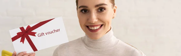 Foto panoramica di una donna sorridente che guarda la macchina fotografica e mostra un buono regalo — Foto stock