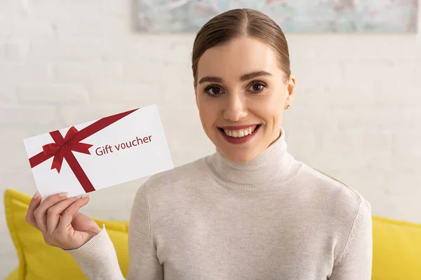 Schöne lächelnde Frau blickt in die Kamera und zeigt Gutschein — Stockfoto