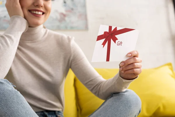 Обрезанный вид улыбающейся девушки с подарочной карточкой на диване — стоковое фото