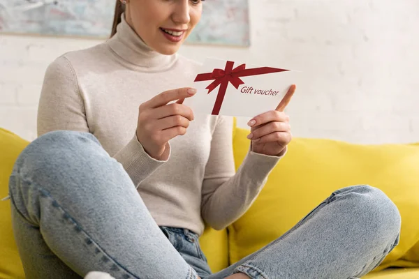 Vue recadrée d'une femme souriante tenant un bon cadeau sur un canapé — Photo de stock