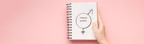 Panoramic shot of woman holding notebook with male and female sign on pink background — Stock Photo