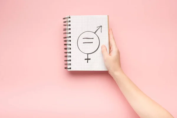 Cropped view of woman holding notebook with male and female sign on pink background — Stock Photo