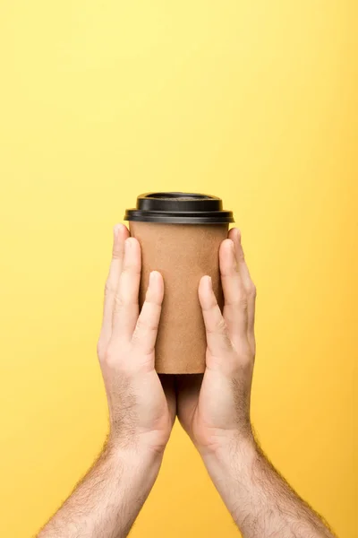 Cropped view of man holding paper cup on yellow background — Stock Photo