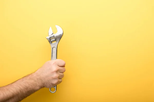 Обрезанный вид человека, держащего гаечный ключ на желтом фоне — стоковое фото