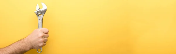 Panoramic shot of man holding spanner on yellow background — Stock Photo