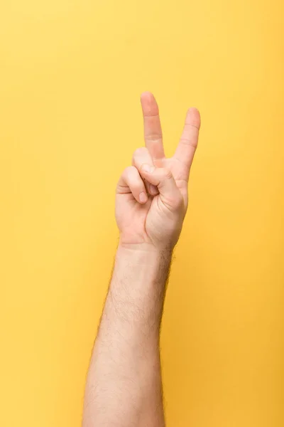 Cropped view of man showing peace gesture on yellow background — Stock Photo