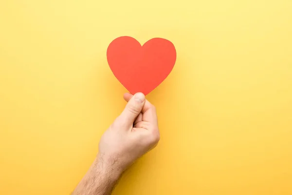 Vista recortada del hombre sosteniendo tarjeta en forma de corazón sobre fondo amarillo - foto de stock