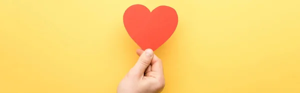 Plano panorámico del hombre sosteniendo tarjeta en forma de corazón aislado en amarillo - foto de stock