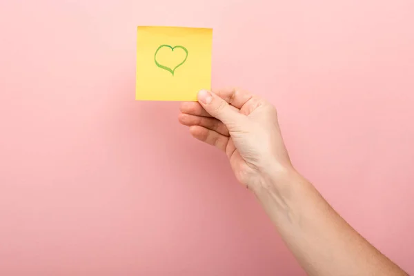 Cropped view of woman holding sticky note with heart on pink background — Stock Photo