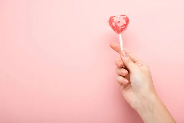 Vista cortada de mulher segurando pirulito em forma de coração no fundo rosa — Fotografia de Stock